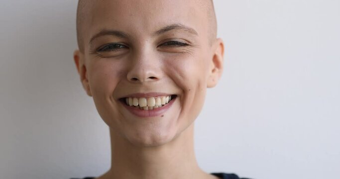 Natural beauty, cancer patient recovery, believe in victory over disease concept. Close up face bald young woman pose on gray studio background having wide charming smile looking at camera feels happy