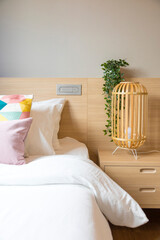 cozy bed in comfort bedroom with white linen, pillows, wicker night lamp on bedside table