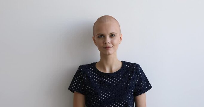 Optimistic bald cancer patient pose on grey background head shot studio portrait. Concept of innovative cancer care and rehabilitation service, girl believe in recovery and oncology disease remission