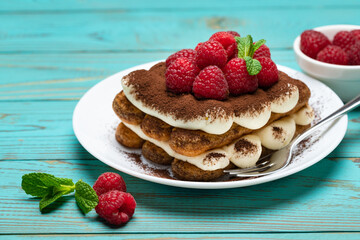 portion of Classic tiramisu dessert with raspberries on blue wooden background