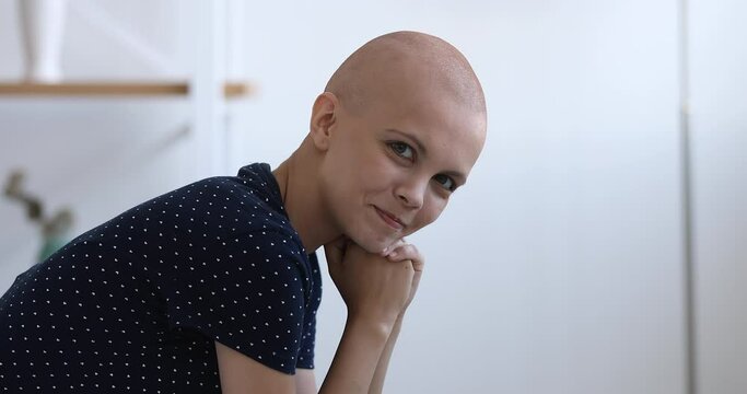 Bald young woman look at camera while sitting indoors. Serious hairless after chemotherapy cancer patient believe in recovery smiling feels hopeful. Oncology disease fighter and rehabilitation concept