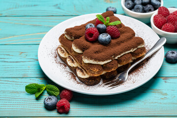 portion of Classic tiramisu dessert with raspberries and blueberries on blue wooden background