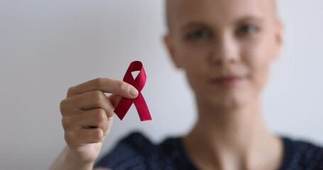 Closeup view bald woman showing to camera red symbolic ribbon posing on grey studio background. World organization participant supporting people with HIV disease, regular check up promotion concept
