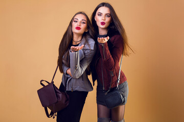 Indoor fashion portrait of two cheerful models, best friends sen kiss posing on beige or orange background . Autumn or winter c concept. Casual trendy clothes. © Svetlana Sokolova