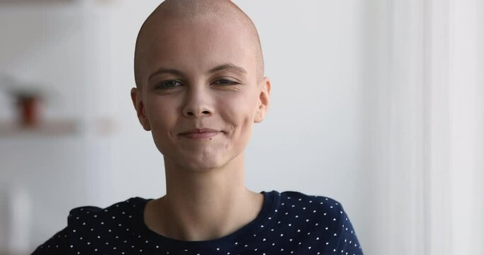 Close up view bald 20s woman standing indoor smile look at camera. Portrait of hairless cancer patient fighter. Remission and recovery, rehabilitation and new day of oncology disease person concept