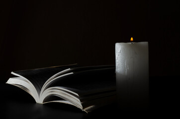 Closeup of opened Bible and candle flame against black background