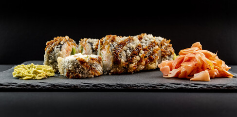 Panoramic photo of served warm sushi with ginger and wasabi on a black stone plate.