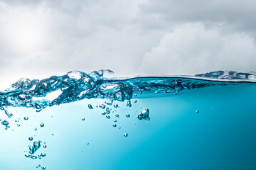 The stormy sea creates strong waves that splash, forming bubbles in the middle of the water against the clouded sky.
