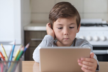 A boy in the kitchen watches a video on a tablet