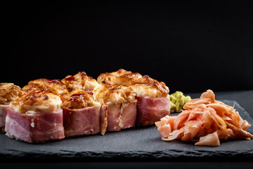 Served warm sushi rolled in bacon with ginger and wasabi on a black stone plate.