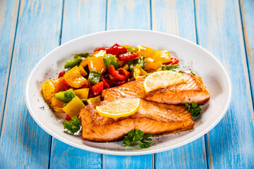 Fried salmon steaks with lemon and bell pepper served on wooden table
