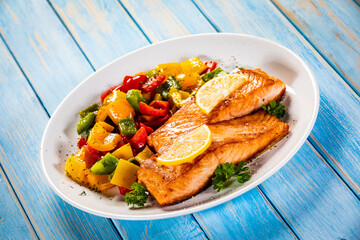 Fried salmon steaks with lemon and bell pepper served on wooden table
