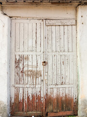Old closed scratched shabby weathered wooden doors with metal door handle of abandoned stone building, and plants with green leaves in front of the door