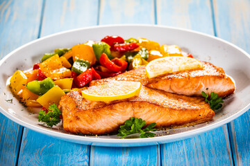 Fried salmon steaks with lemon and bell pepper served on wooden table
