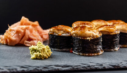 Served warm sushi rolled in nori sheets with ginger and wasabi on a black stone plate.