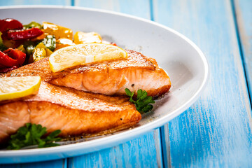 Fried salmon steaks with lemon and bell pepper served on wooden table
