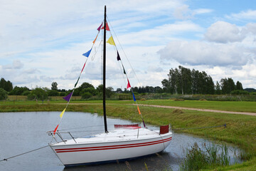 Small white yacht with colorful flags in small lake or pond used as landscape decoration in amusement park .
