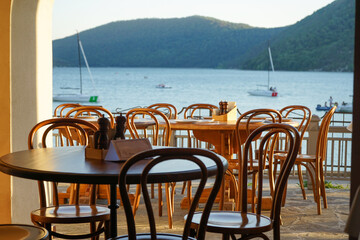view from the street with tables and chairs to a mountain lake, sailboats and mountains at sunset