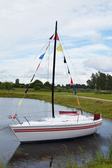 Small white yacht with colorful flags in small lake or pond used as landscape decoration in amusement park .
