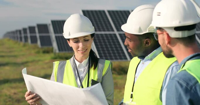 Three technical engineers review plan on paper and discuss. Two men listen to woman's explanations about nuances of work.