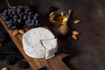 Camembert or brie french soft cheese with grapes, honey, nuts and berries on wooden background.