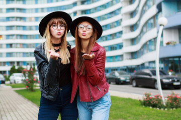 Couple of two stylish woman in trendy spring outfit sending air-kiss to camera .  Wearing leather...