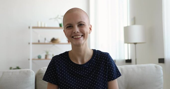 Bald female sit on sofa start videocall, talk to friend share experience about oncology disease and healing feels overjoyed looking at camera. Cancer survivor and video call event with doctor concept