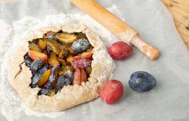  On white baking paper fruit biscuit ripe plums flour and rolling pin. Cooking plum cake.