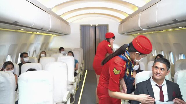 women with face mask flight attendant or cabin crew is walking and checking passengers seat and equipment in airplane. Concept new traveling for healthcare protocols and prevent virus pandemic.
