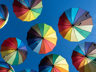 Two decorative colorful umbrellas hanging on ropes in the air on blue sky background. Horizontal picture