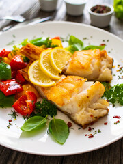 Fish dish - fried cod fillet with fried vegetables and lemon served on wooden table