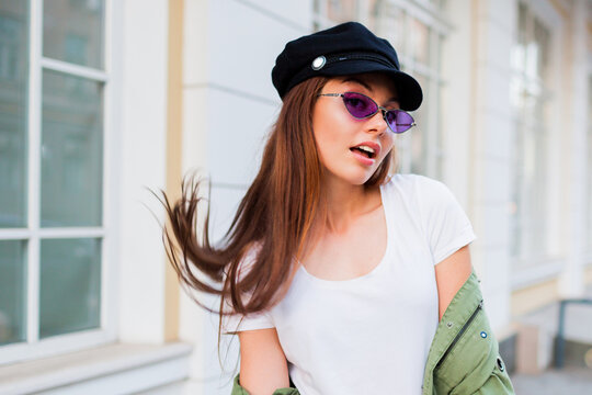 Happy brunette weoman posing outdoor . Stylish hat, sunglasses and green jacket.