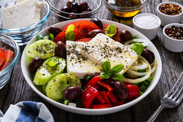 Fresh Greek salad - feta cheese, tomatoes, cucumber, red pepper, black olives and onion on wooden table
