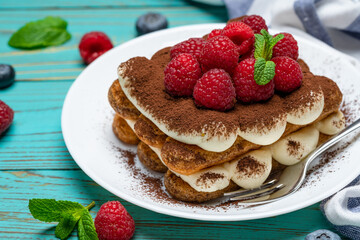 portion of Classic tiramisu dessert with raspberries and blueberries on blue wooden background