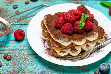 portion of Classic tiramisu dessert with raspberries and blueberries on blue wooden background