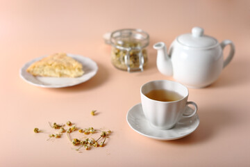 Fototapeta na wymiar White cup with brewed chamomile, teapot, pie and jar of tea on a pink background.