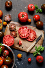 Fresh colorful ripe fall or summer heirloom variety tomatoes with knife and chopping board over dark blue table background. Harvest and cooking tomato sauce concept.