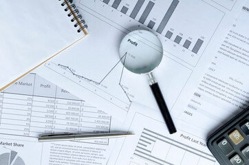 Top view of magnifying glass, pen, calculator, notebook and lot of business documents with charts,...