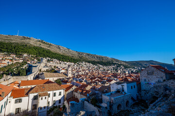 Fototapeta na wymiar Colorful fortress street walk scene, clear sky sunny day. Beautiful building roofs. Scenery winter view of Mediterranean old city of Dubrovnik, famous European travel and historic destination, Croatia