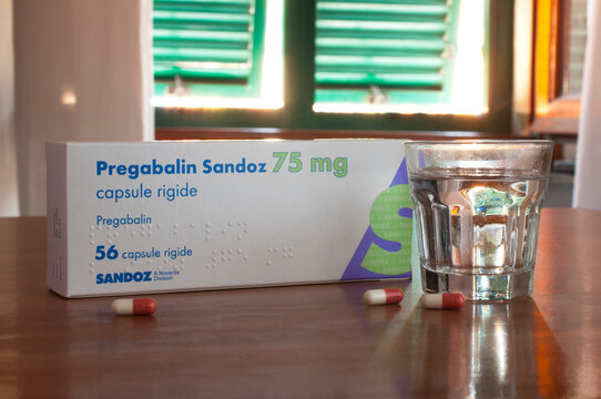 A box and some pills of Pregabalin on a table with a glass of water. Pregabalin is a medicine to treat epilepsy and anxiety.