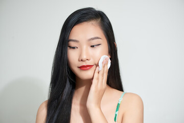 Pretty beauty young Asian woman cleaning her face with cotton pad over white isolated background. Healthy skin and cosmetics concept.