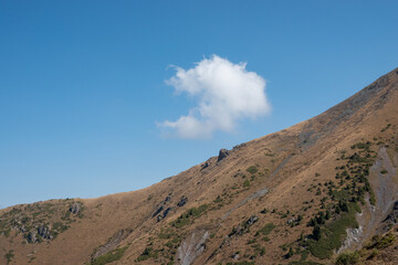 Landscape with a blue sky, white cloud and a brown hill