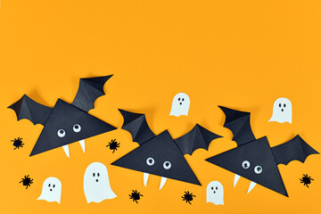 Cute paper vampire bats with googly eyes and ghosts and spiders on orange Halloween background with...