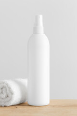 Obraz na płótnie Canvas White cosmetic bottle spray mockup with a towel on a wooden table.