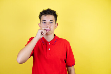 Beautiful teenager boy over isolated yellow background mouth and lips shut as zip with fingers....