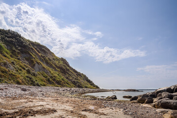 Fototapeta na wymiar Steilküste mit Steinstrand im Gegenlicht , blauem Himmel mit leichten Wolken und Meer, Dänemark