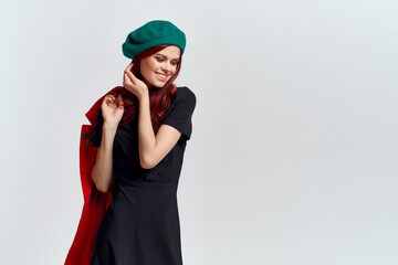 Naklejka premium A woman holds in her hand a red coat and a dark T-shirt Green hat cropped view of a light background