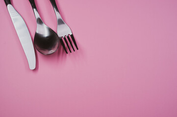High angle shot of a spoon, fork, and knife on a pink surface
