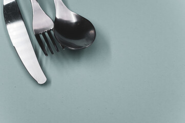 High angle shot of a spoon, fork, and a knife on a grey surface