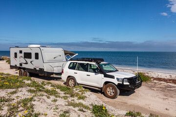 Landscape view of 4WD and modern caravan parked adjacent to a sparkling sunny beach. - obrazy, fototapety, plakaty